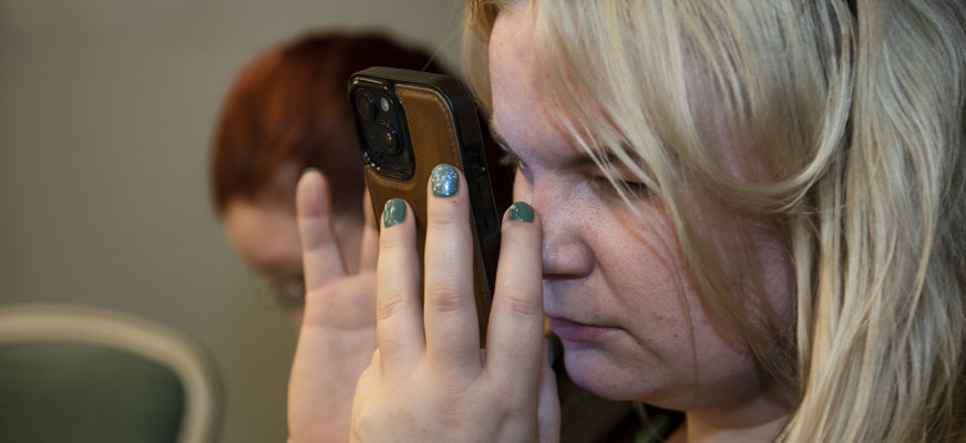 Blond kvinna tittar mycket nära på smartphone.