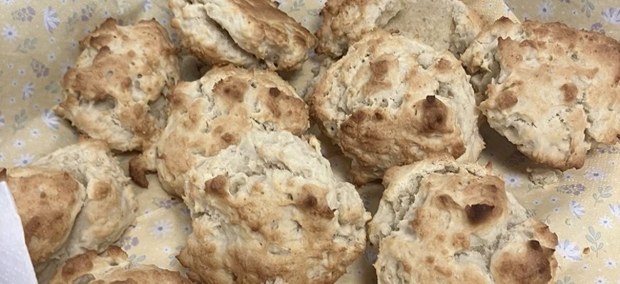 Nybakade scones ligger på gula servetter med lila och vita blommor i en korg av rotting