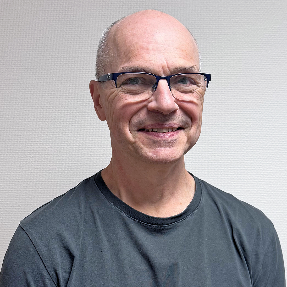Porträttbild på Norbert, en medelålders man. Norbert är blåögd, tunnhårig och renrakad. Han bär glasögon med svarta bågar och en grå t-shirt. Norbert ler mot kameran.