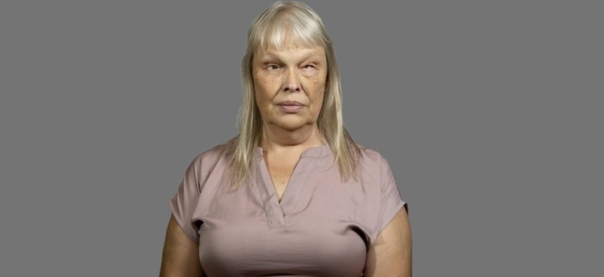 En närbild av en kvinna i 50-års-åldern som tittar rakt fram. Hon har långt, ljust hår med lugg och ett neutralt ansiktsuttryck. Bakgrunden är ljus och avskalad.