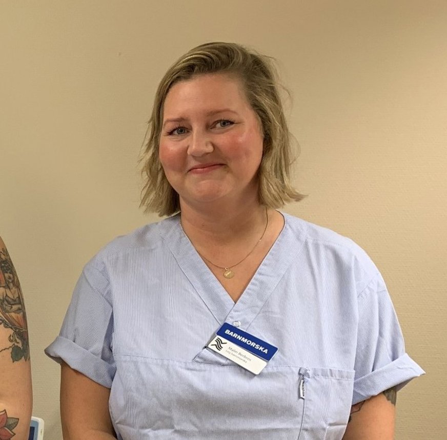 Malin Berbres i kort, blont hår iklädd kortärmad skjorta. Hon har en namnskylt där det står "Barnmorska".