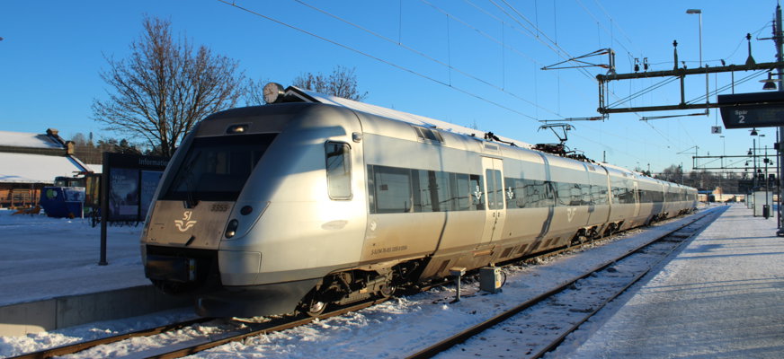 Ett tåg vid en snöig perrong. Blå himmel i bakgrunden.