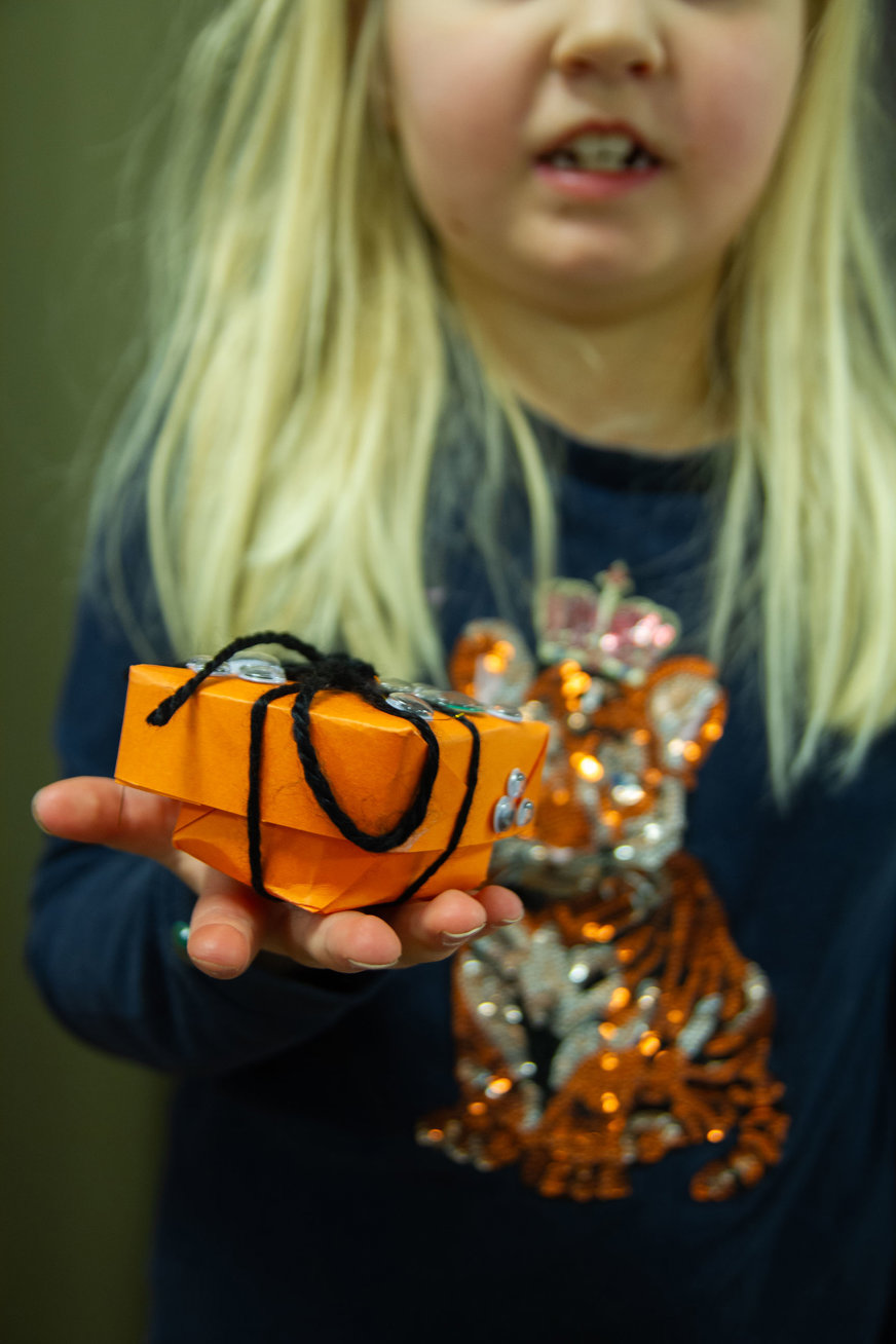 Närbild blond flicka håller upp orange papperslåda med svart snöre och låtsasögon
