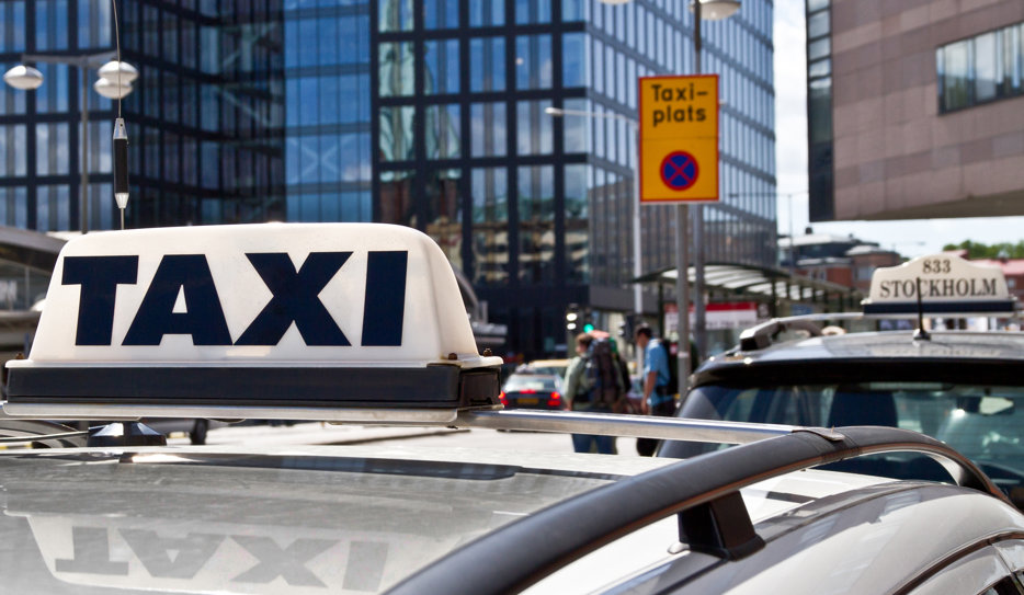 Taket på en taxibil i stadsmiljö. I bakgrunden syns höghus, fler bilar och människor.