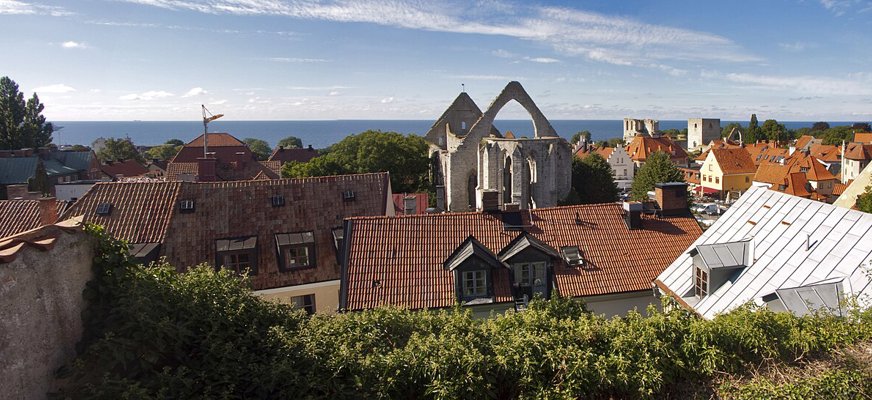 En panoramabild över nedre Visby i solsken. Havet skymtar längst bort och den ikoniska ruinen över klosterkyrkan Sankta Karin reser sig över hustaken. Foto: Alexandru Baboş Albabos