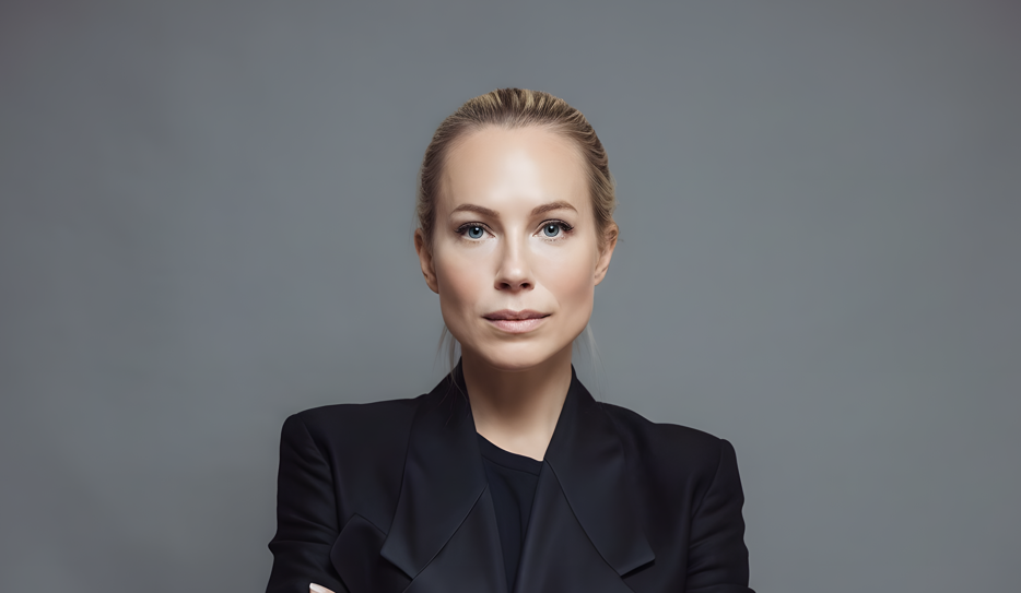 Anna Quarnström står med armarna i kors och tittar rakt in i kameran. Hon är klädd i svart kavaj och har sitt blonda hår uppsatt i en knut i nacken.