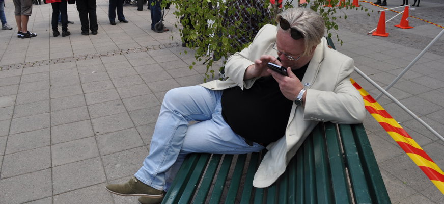 Man på parkbänk försjunken i smartphone som han håller mycket nära ansiktet.