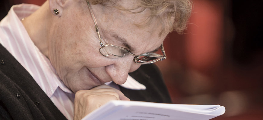 Äldre kvinna läser, håller A4-papper mycket nära och kisar.