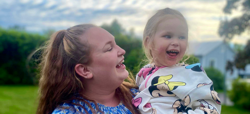 Mamma Lilly håller i dottern Lovi. De skrattar tillsammans åt något ur bild som Lovi tittar mot.