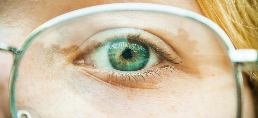 Närbild på ett grönt öga bakom glasögon med stålbågar.