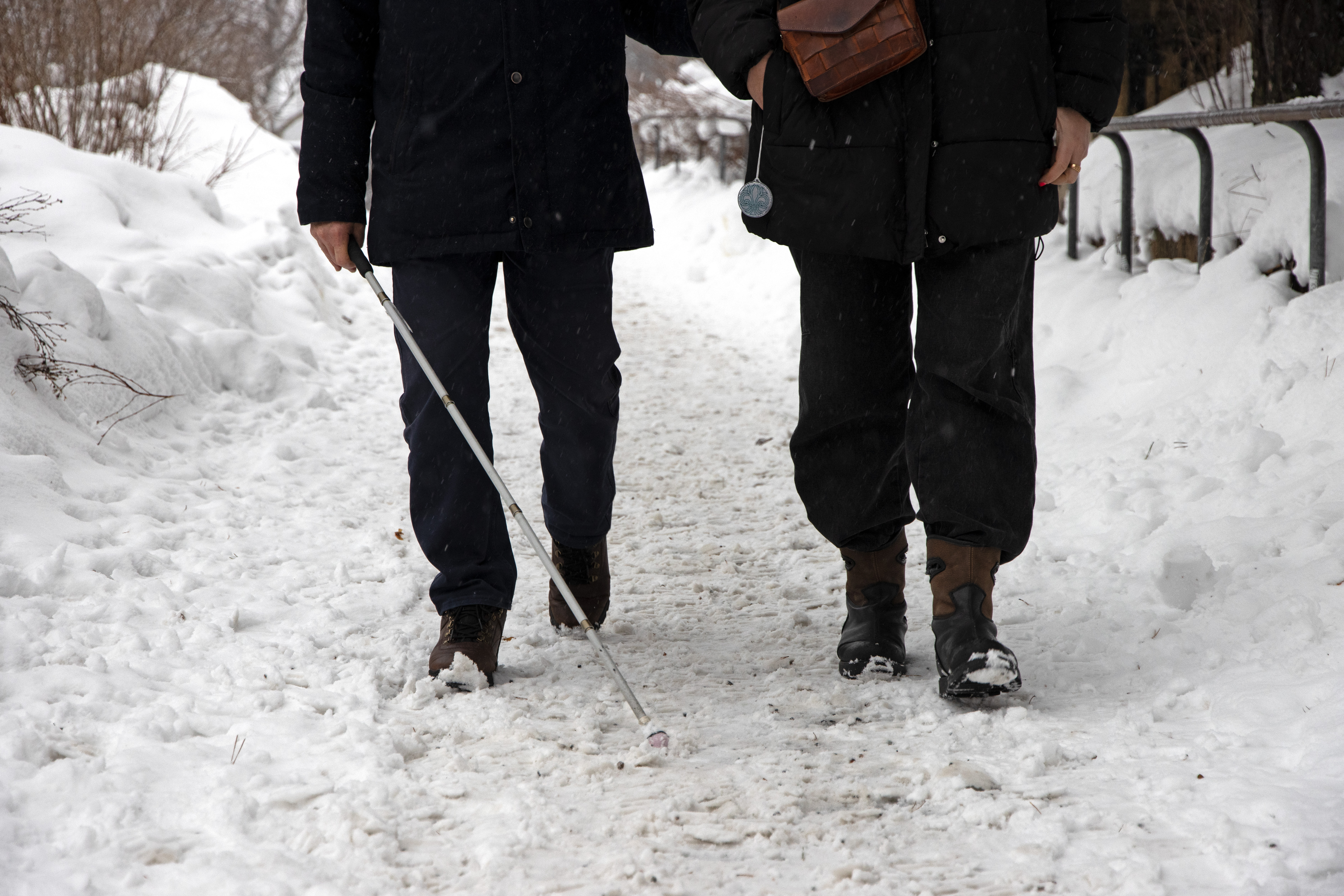 En person med vit käpp blir ledsagad i snöigt landskap. 