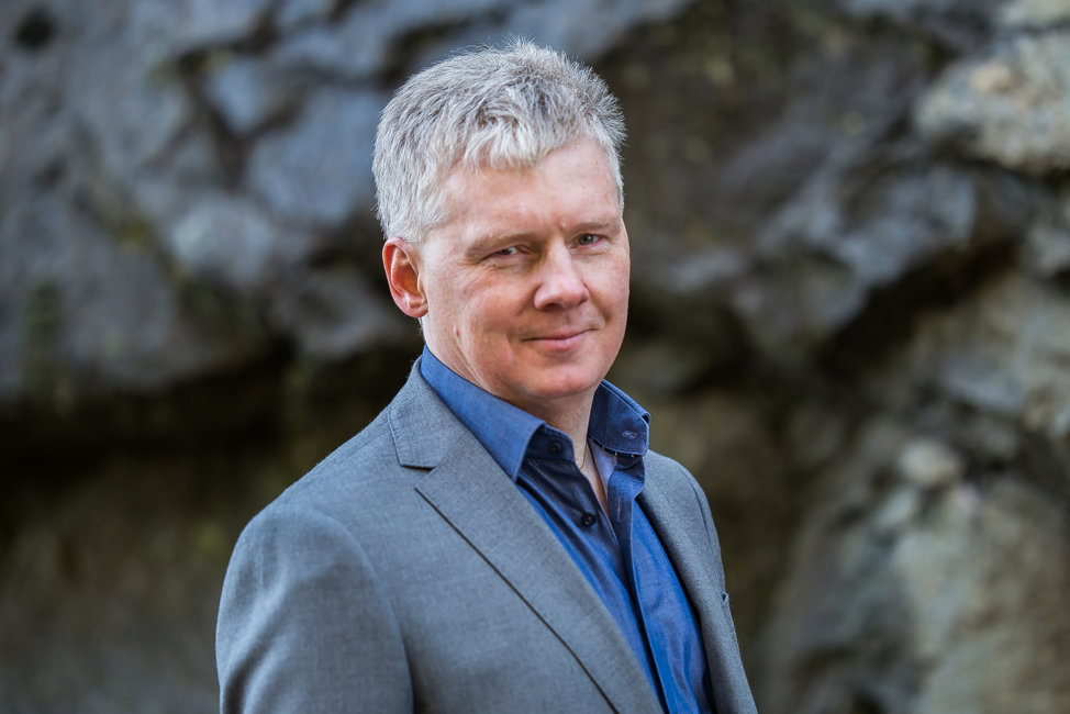 Niklas Mattsson i grå kostym, blå skjorta framför bergvägg.
