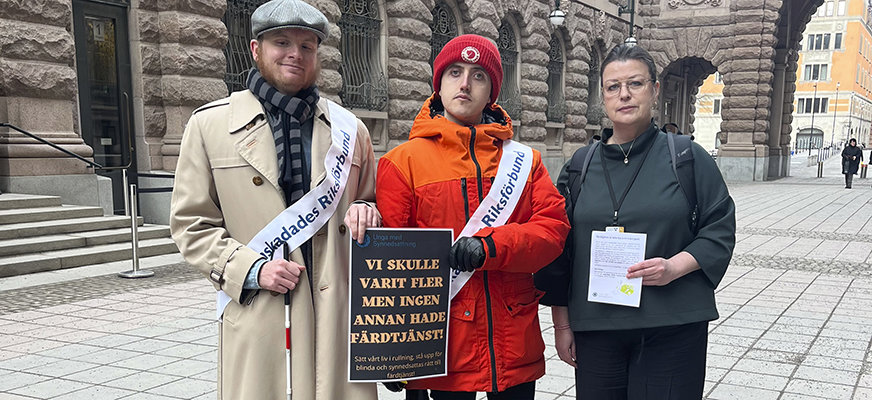 Tre personer utanför riksdagen, båda med gehäng med Synskadades Riksförbunds logotyp på. En med vit käpp. De håller i en skylt "Vi skulle varit fler men ingen annan hade färdtjänst".