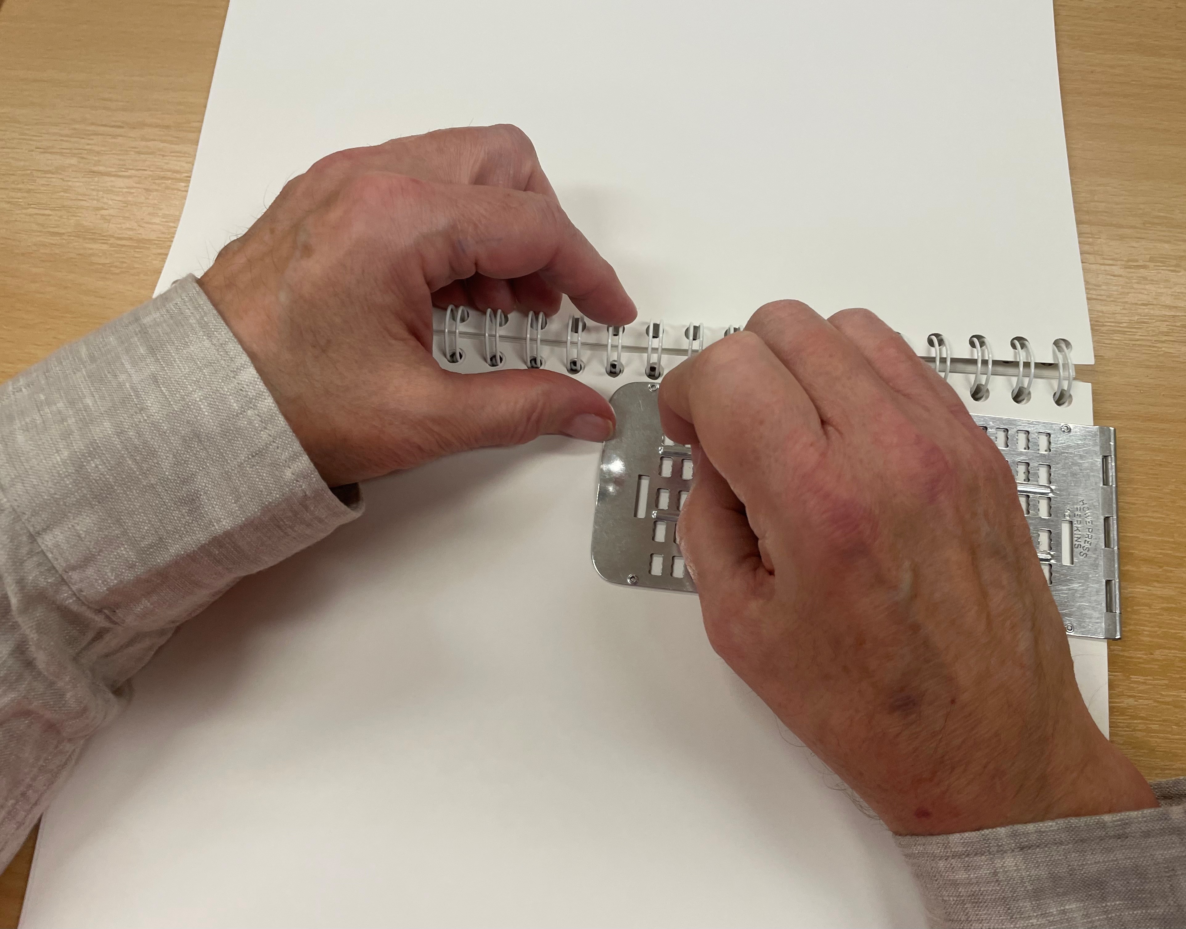 Händer som skriver punktskrift för hand med reglett och syl.